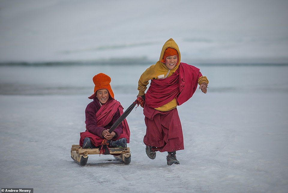 Two young monks enjoy some downtime by playing on a sledge on a frozen river bank in Zanskar